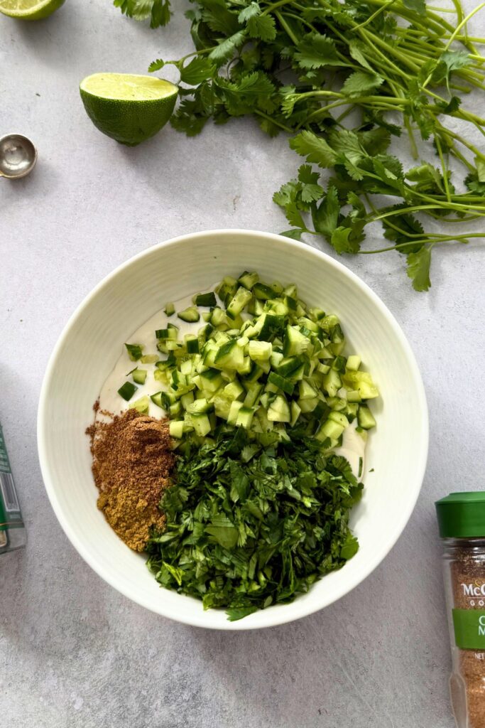 vegan cucumber raita ingredients with persian cucumbers, cilantro, dairy free yogurt, cumin and garam masala